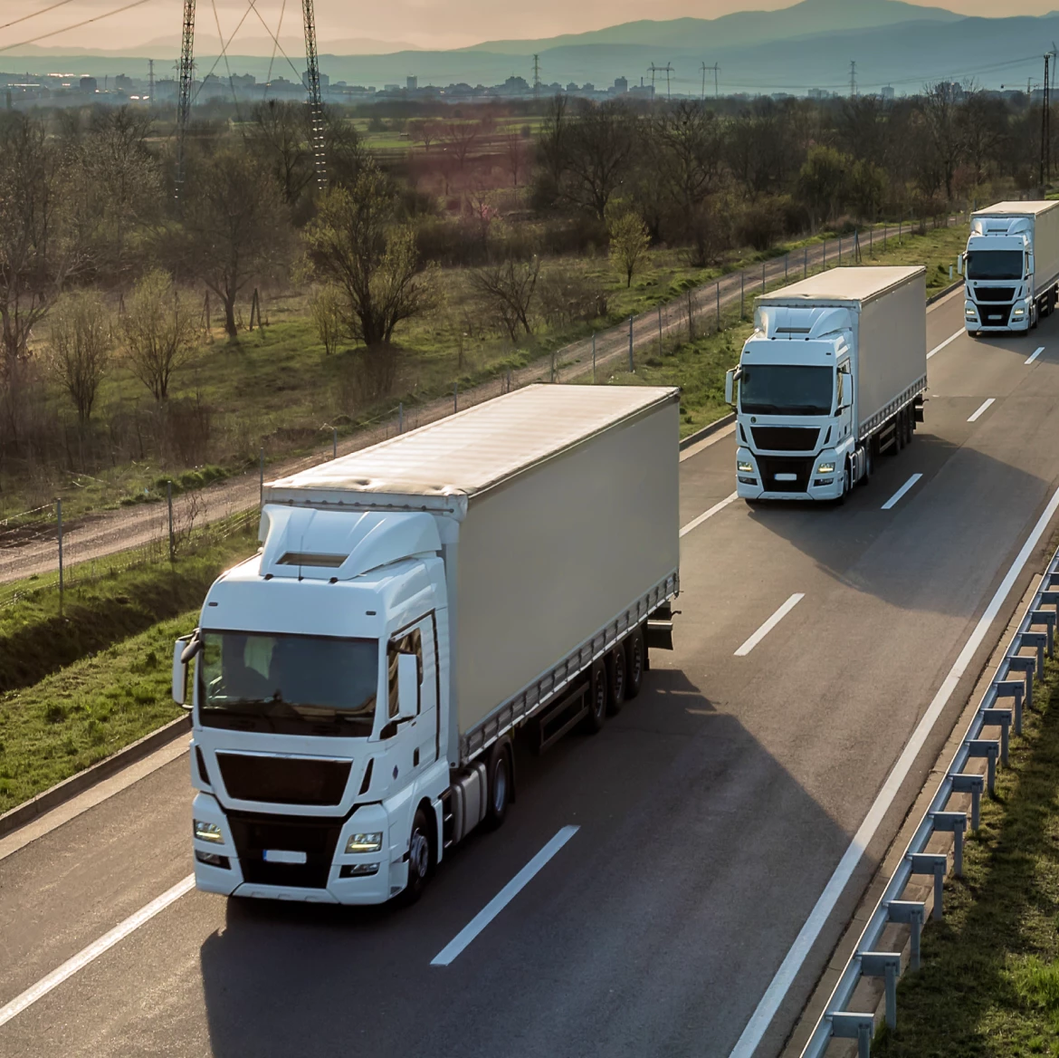 Three white semi-trailer trucks driving on the highway.