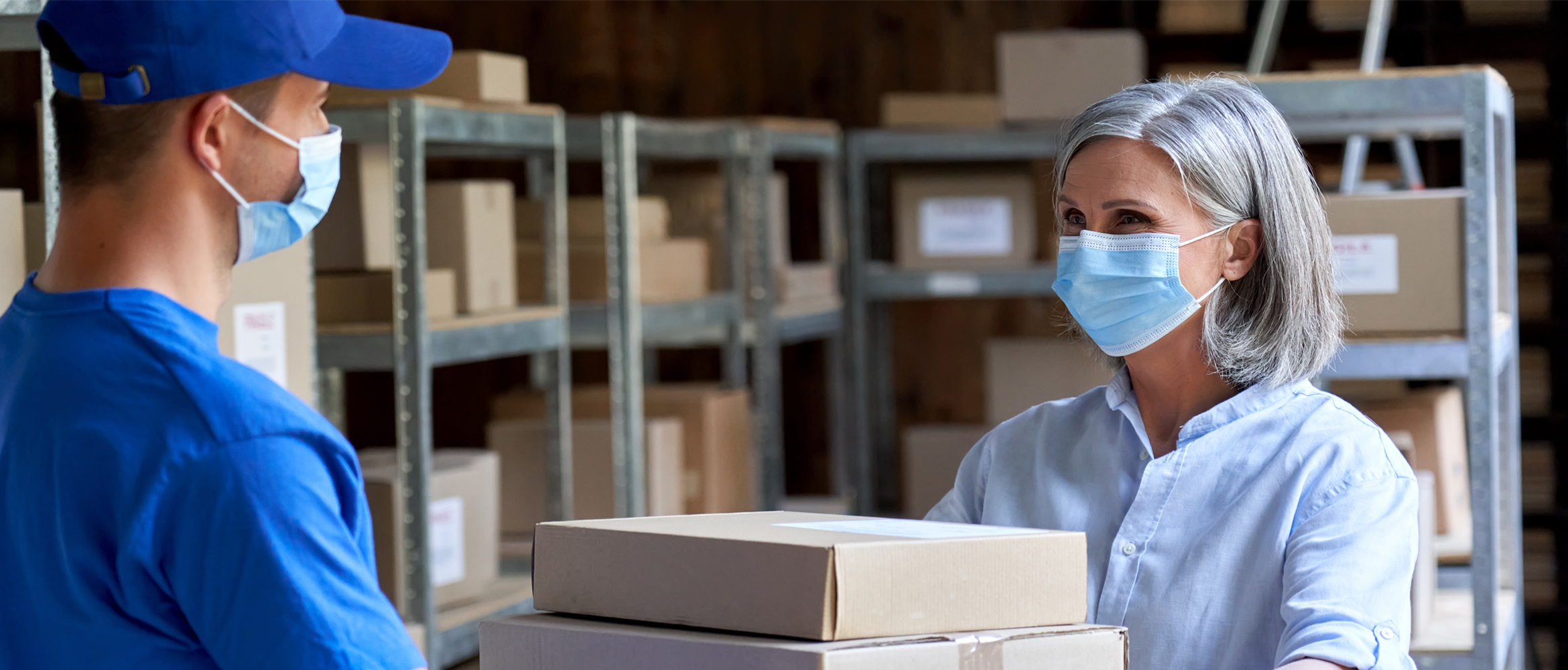 A logistics worker and a colleague wearing masks in a warehouse organizing cargo.