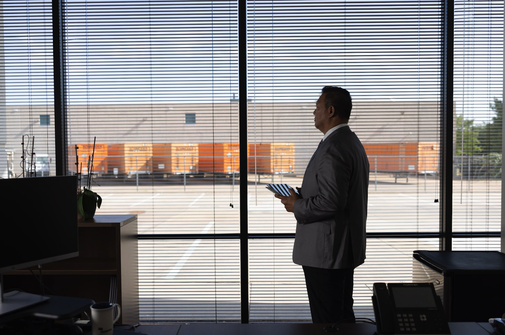 A Morrison employee in his office looking out the window at the trucks and warehouse symbolizing a commitment to service excellence and tailored logistics solutions for clients.