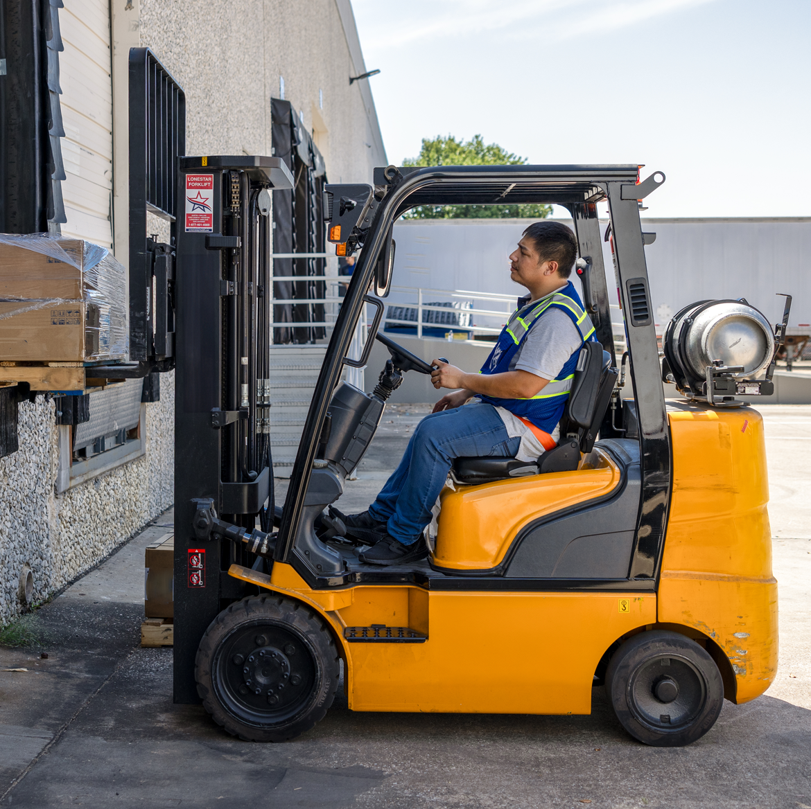 A Morrison warehouse worker operating a forklift outside the warehouse, unloading cargo.