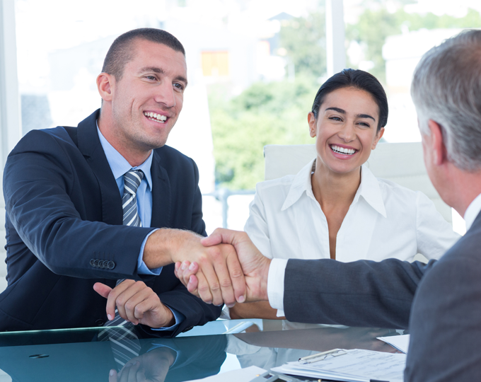 " Two business partners handshaking across the conference table. "